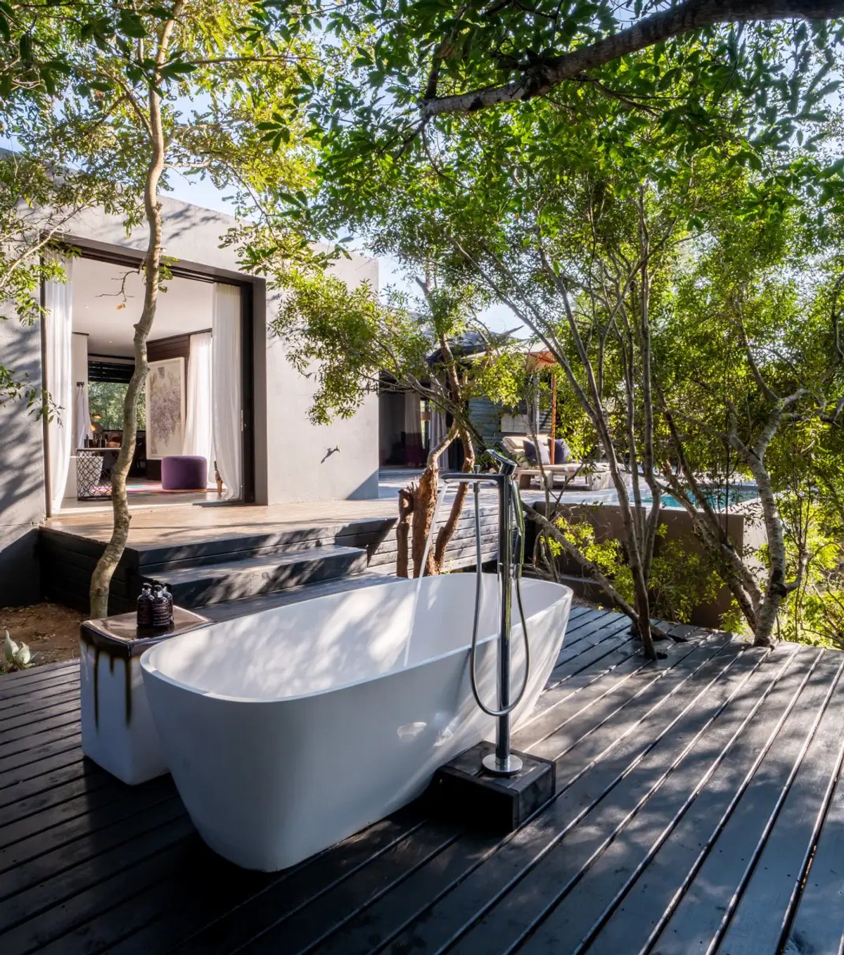 A modern bathtub is situated outdoors, surrounded by lush greenery and a wooden deck, providing a serene and luxurious atmosphere at Silvan Safari.