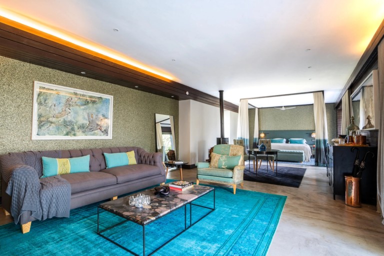 The interior of the Blue Guarri Suite at Silvan Safari, showcasing a modern lounge area with a plush couch, detailed decor, and a view of the bedroom area.