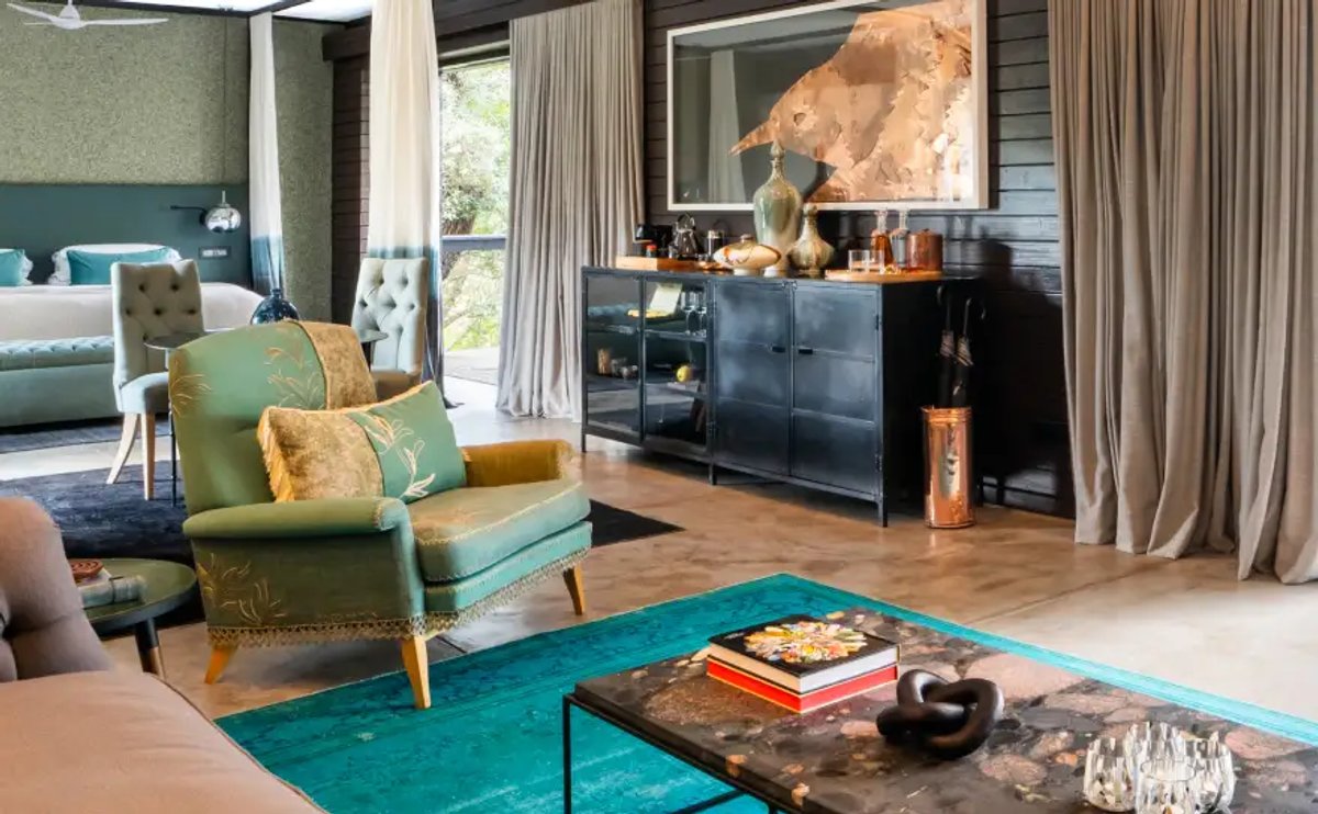The image features a beautifully designed lounge area at Silvan Safari, showcasing a mix of modern and stylish furnishings, including a green armchair, plush bedding, and decorative accents.