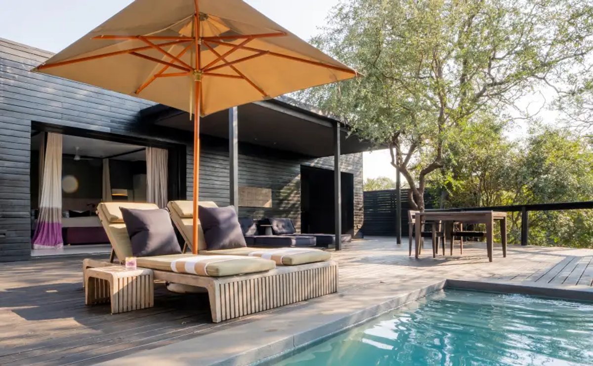 A tranquil pool area at Silvan Safari Lodge featuring lounge chairs, an umbrella, and beautiful landscaping in a serene outdoor setting.