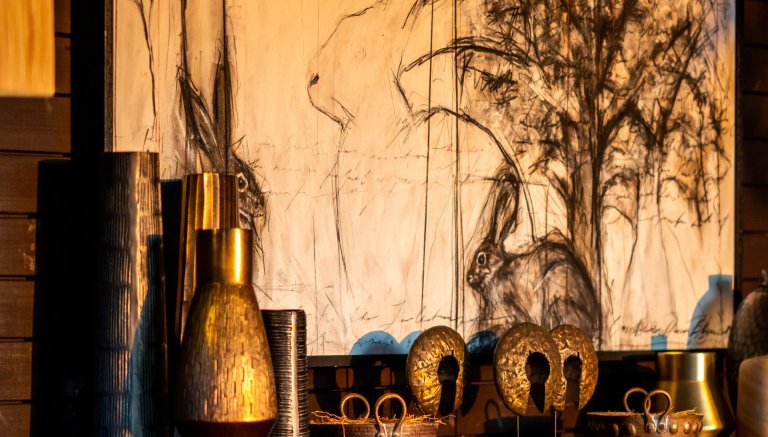 The image features an artistic display with stylized drawings of rabbits on a wall, surrounded by various decorative vases and sculptures, indicative of an elegant lodge setting.