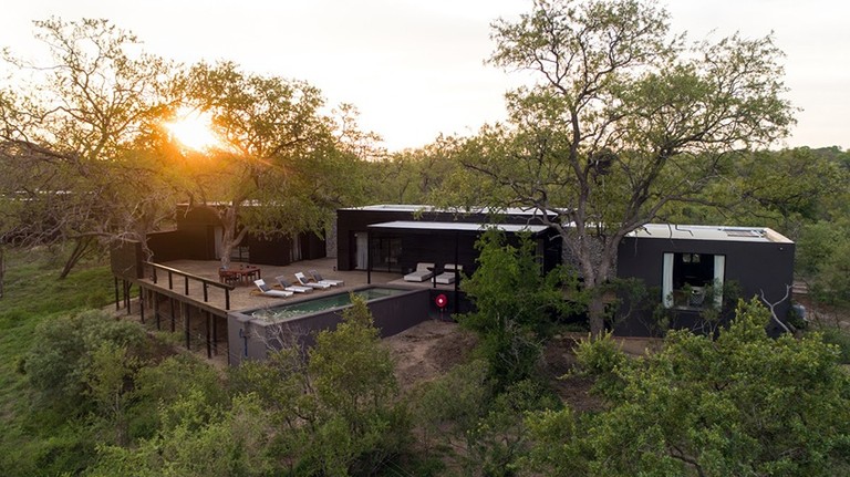Aerial view of Silvan Safari Lodge, showcasing its modern architecture surrounded by lush greenery at sunset.