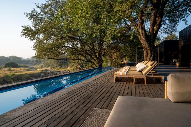 Silvan Safari Lodge Poolside View The image showcases a serene poolside view at Silvan Safari Lodge, featuring lounge chairs placed along the deck with lush greenery and a tranquil landscape in the background.