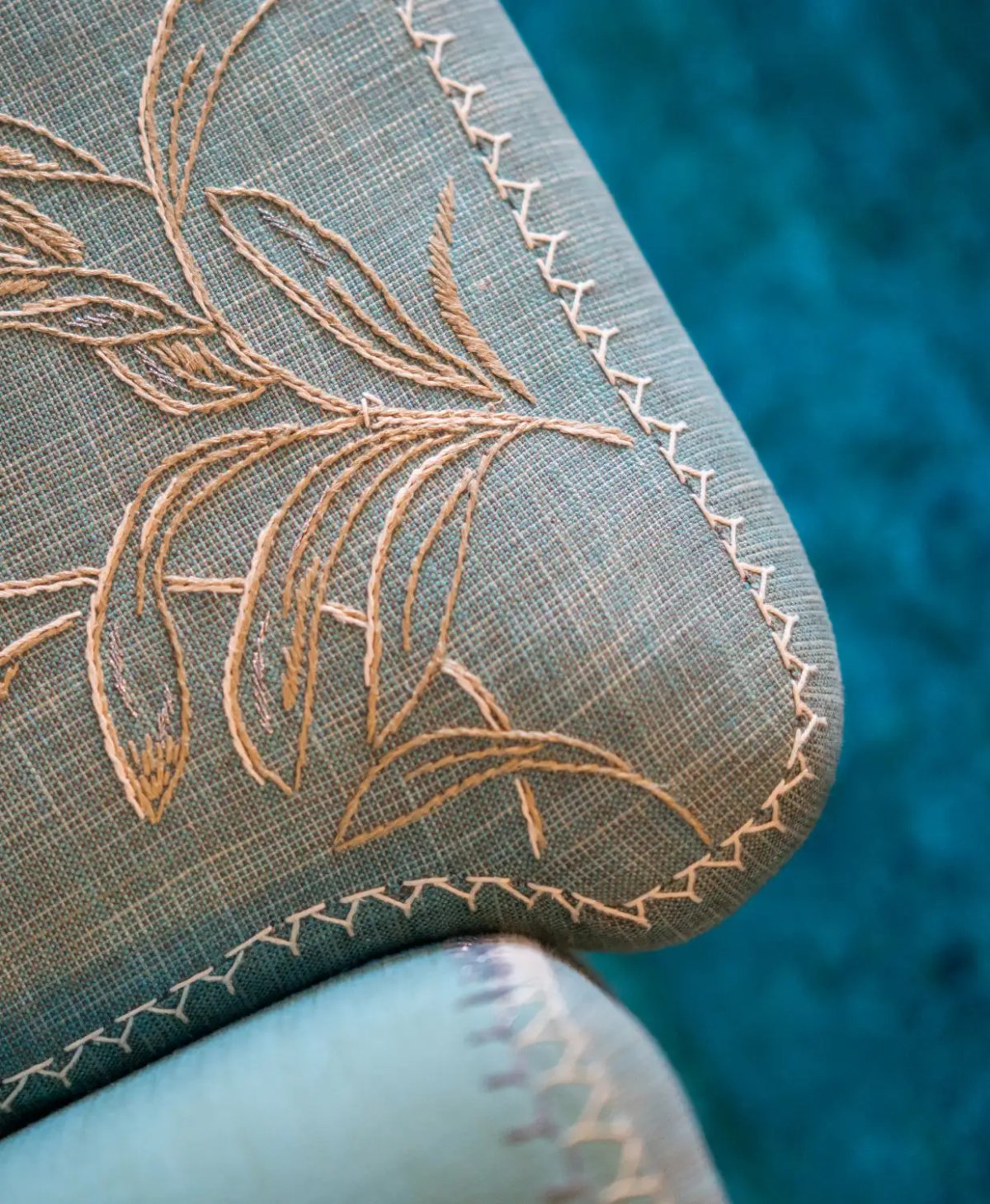 The image features the intricate embroidery and stitching details on upholstered furniture, predominantly in shades of teal and beige.