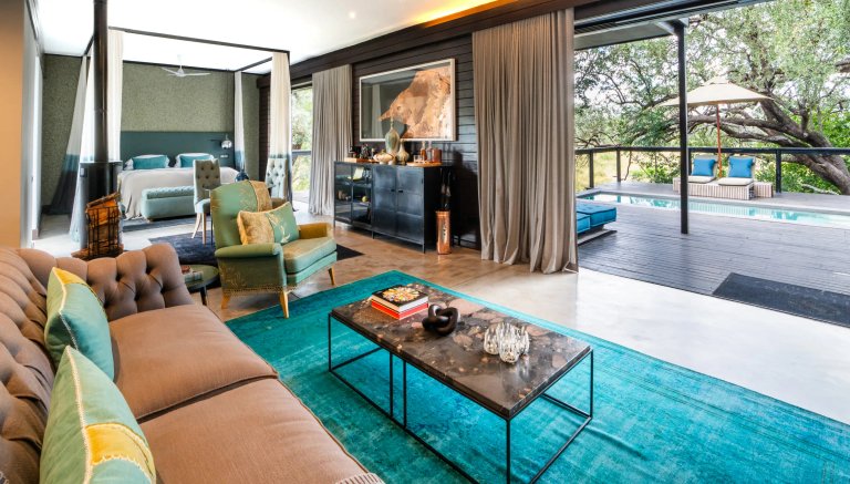 The image showcases a stylishly decorated lodge room featuring a spacious living area with elegant furniture, a bed in the background, and a view of the outdoor pool area.