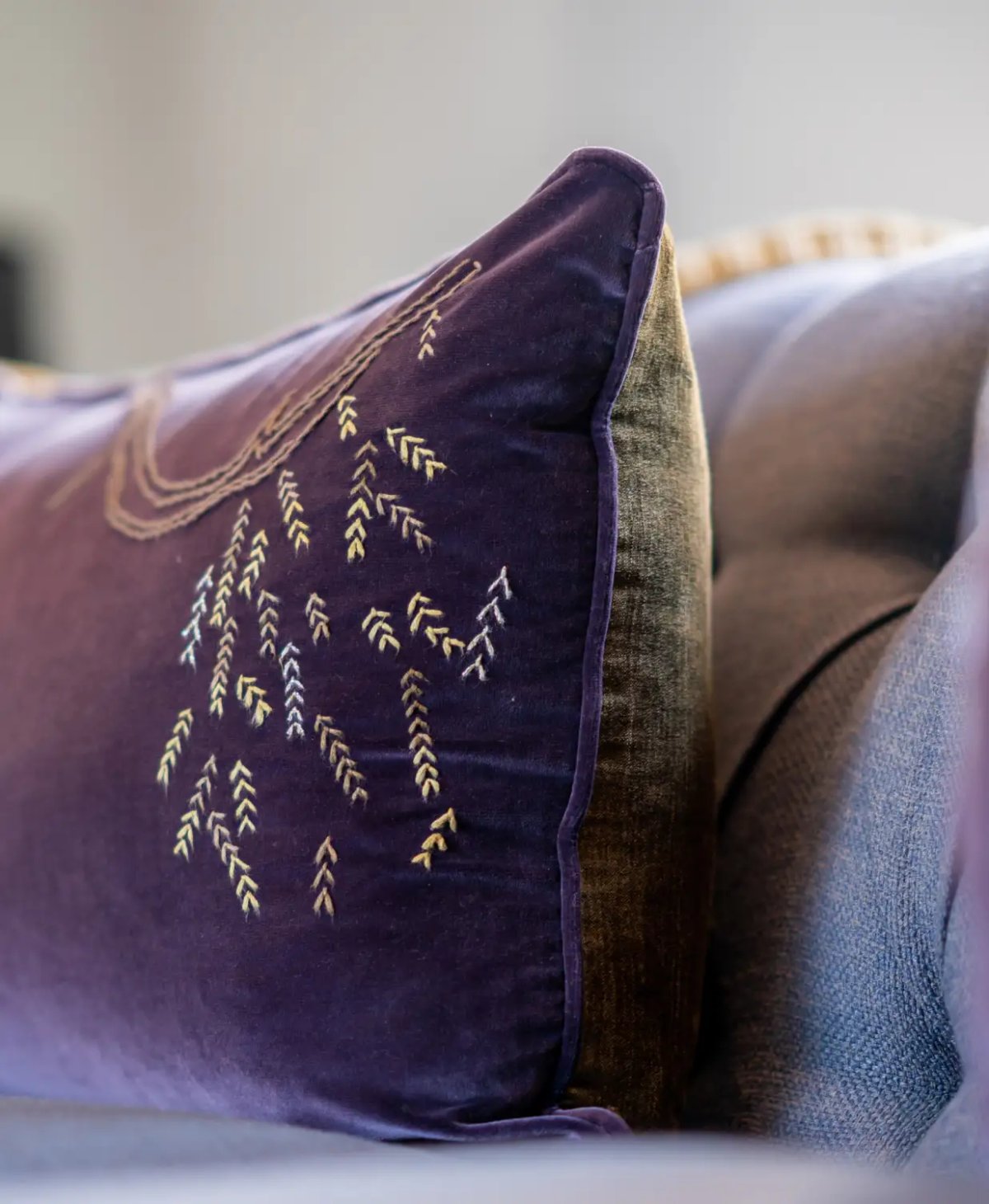 This image features a close-up of a decorative pillow with intricate embroidery on a velvet background, highlighting the textured designs in shades of purple and gold.