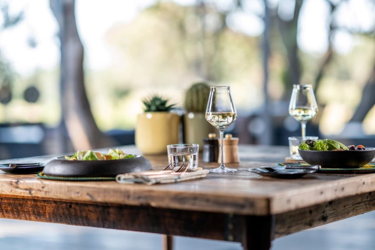 Dining Table Setup A beautifully arranged dining table with salads, glasses of white wine, and decorative plants in the background, presenting a serene dining experience.
